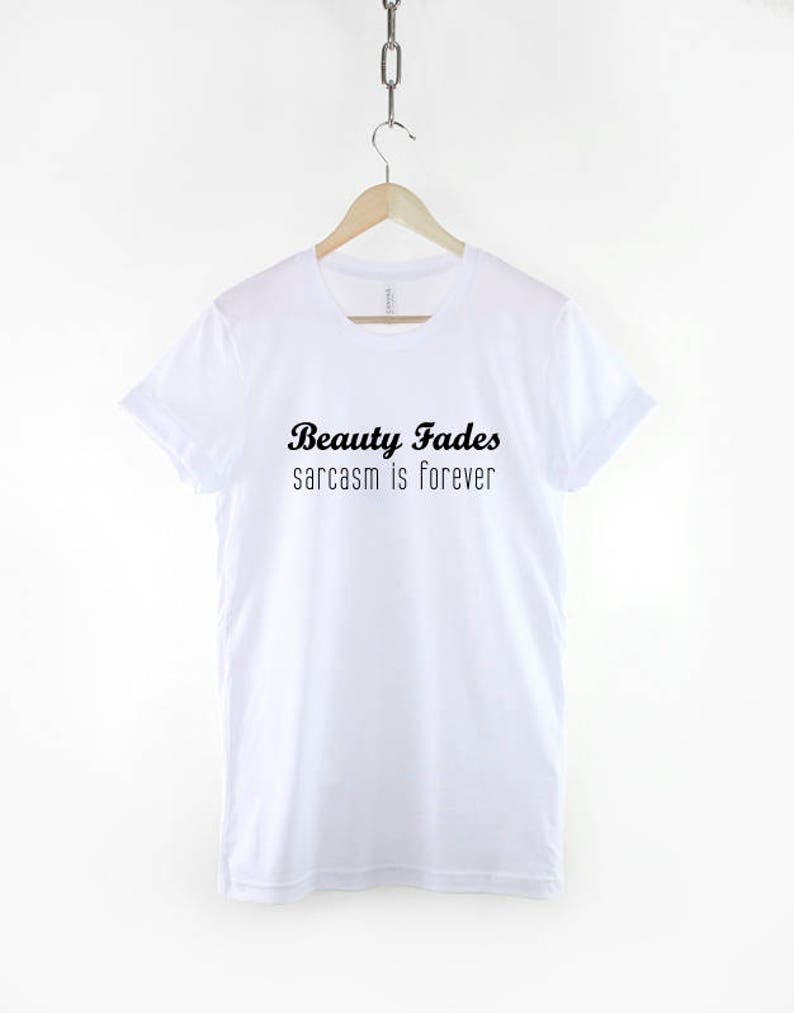 May include: White t-shirt with black text that reads "Beauty Fades sarcasm is forever".