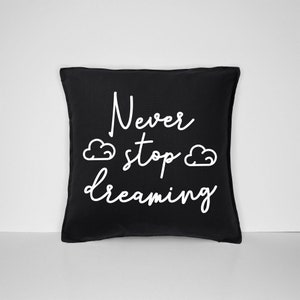 May include: Black throw pillow with white text that reads "Never stop dreaming" and two white cloud illustrations.