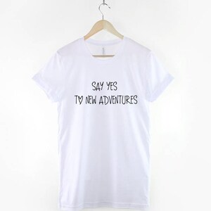 May include: White t-shirt with black text that reads "Say yes to new adventures".