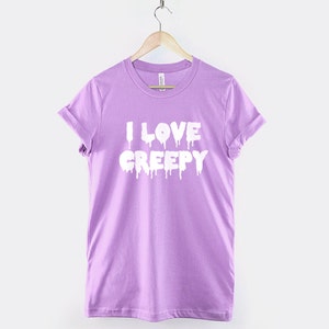 Puede incluir: Una camiseta de color lavanda con el texto "I LOVE CREEPY" en letras blancas que gotean.