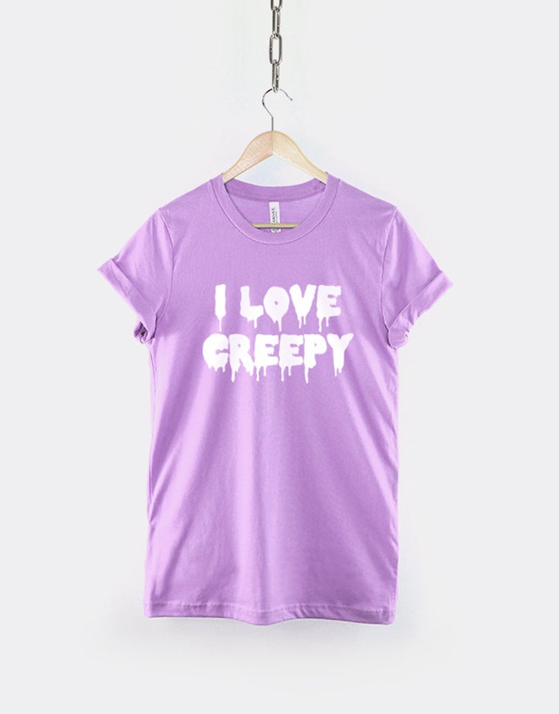 Puede incluir: Una camiseta de color lavanda con el texto "I LOVE CREEPY" en letras blancas que gotean.