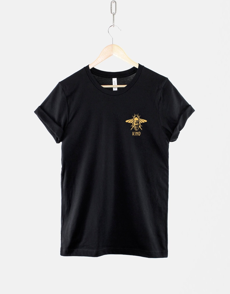 Op de afbeelding: Zwart T-shirt met een gouden bij-print en het woord "KIND" eronder.