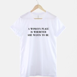May include: White t-shirt with the text "A woman's place is wherever she wants to be."