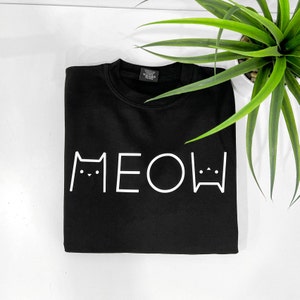 May include: Black t-shirt with a white graphic of the word "MEOW" with cat faces on either side.