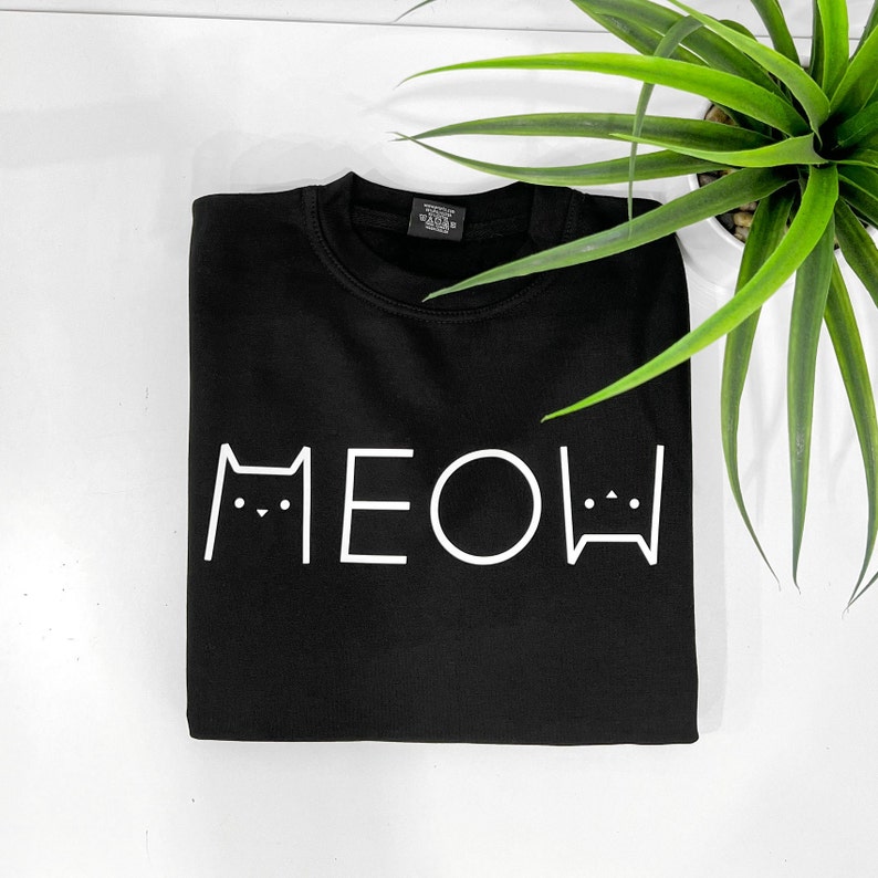 May include: Black t-shirt with a white graphic of the word "MEOW" with cat faces on either side.