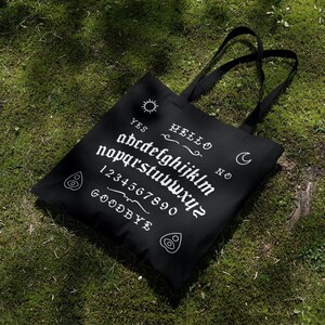 May include: Black tote bag with a white ouija board design. The design includes the letters of the alphabet, numbers 1-0, and the words "YES", "NO", "HELLO", and "GOODBYE".
