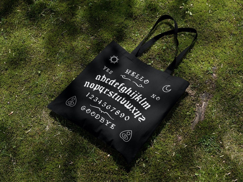 May include: Black tote bag with a white ouija board design. The design includes the letters of the alphabet, numbers 1-0, and the words "YES", "NO", "HELLO", and "GOODBYE".