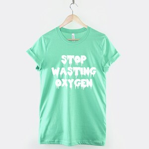 May include: A light green t-shirt with a white graphic that says "Stop Wasting Oxygen" in dripping letters.