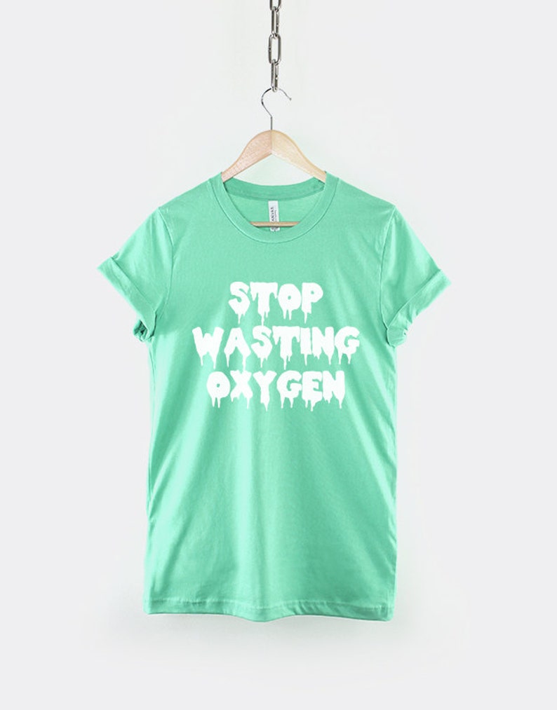 May include: A light green t-shirt with a white graphic that says "Stop Wasting Oxygen" in dripping letters.