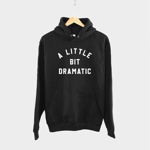 May include: Black hooded sweatshirt with the text "A LITTLE BIT DRAMATIC" printed in white.