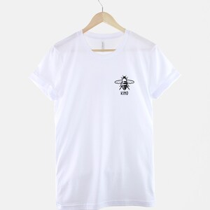 Op de afbeelding: Wit T-shirt met een zwarte bij-afbeelding en het woord "KIND" eronder.