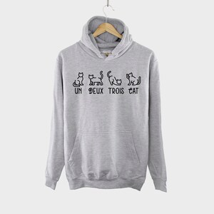 May include: A gray hooded sweatshirt with a black graphic of cats and the text "UN DEUX TROIS CAT".