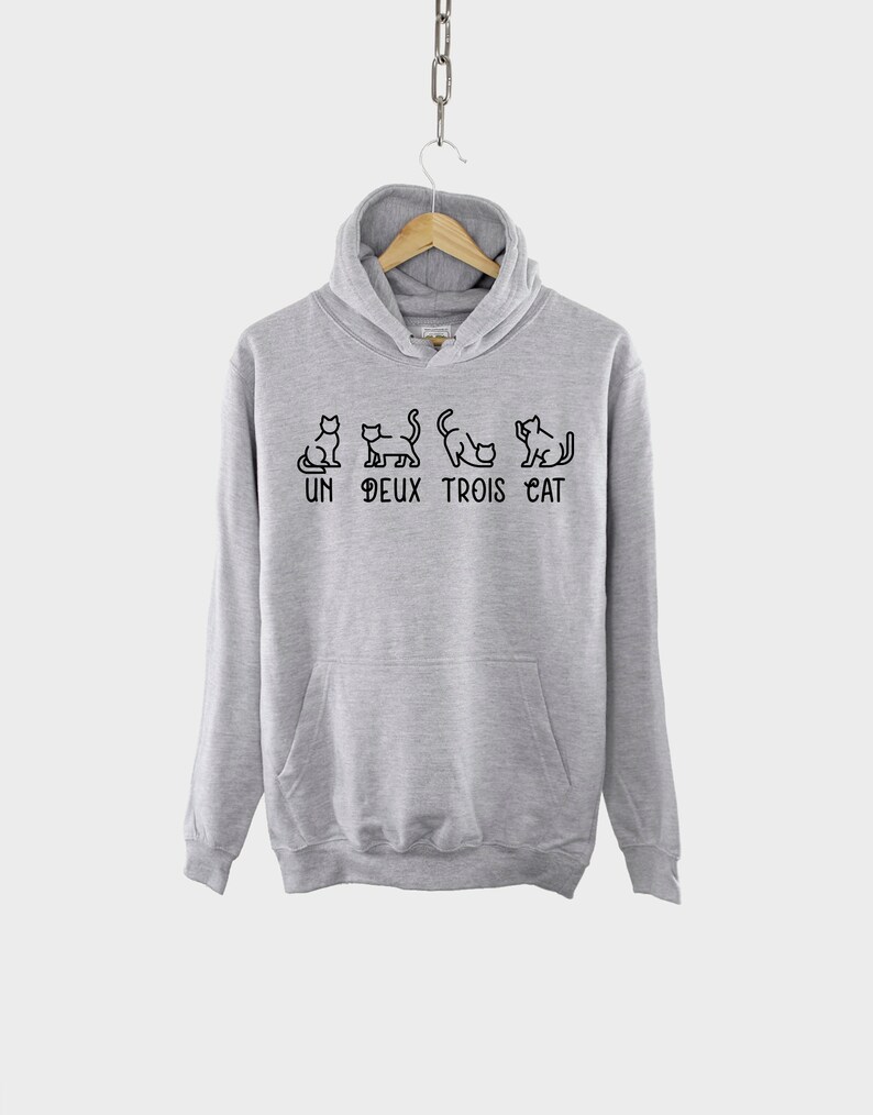 May include: A gray hooded sweatshirt with a black graphic of cats and the text "UN DEUX TROIS CAT".