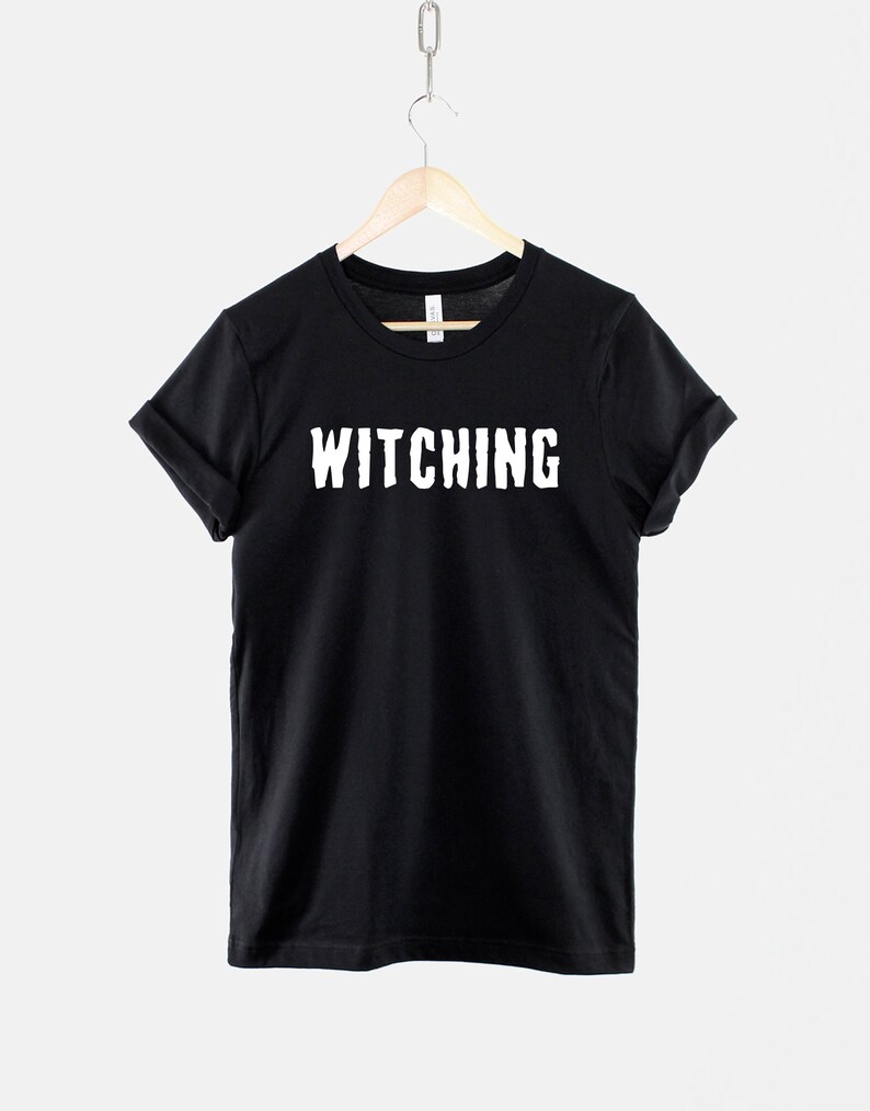 May include: Black t-shirt with white text that reads "Witching" on a black hanger.