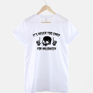 Peut inclure: T-shirt blanc avec un motif de cr&acirc;ne et d'os crois&eacute;s noirs et le texte "It's never too early for Halloween".