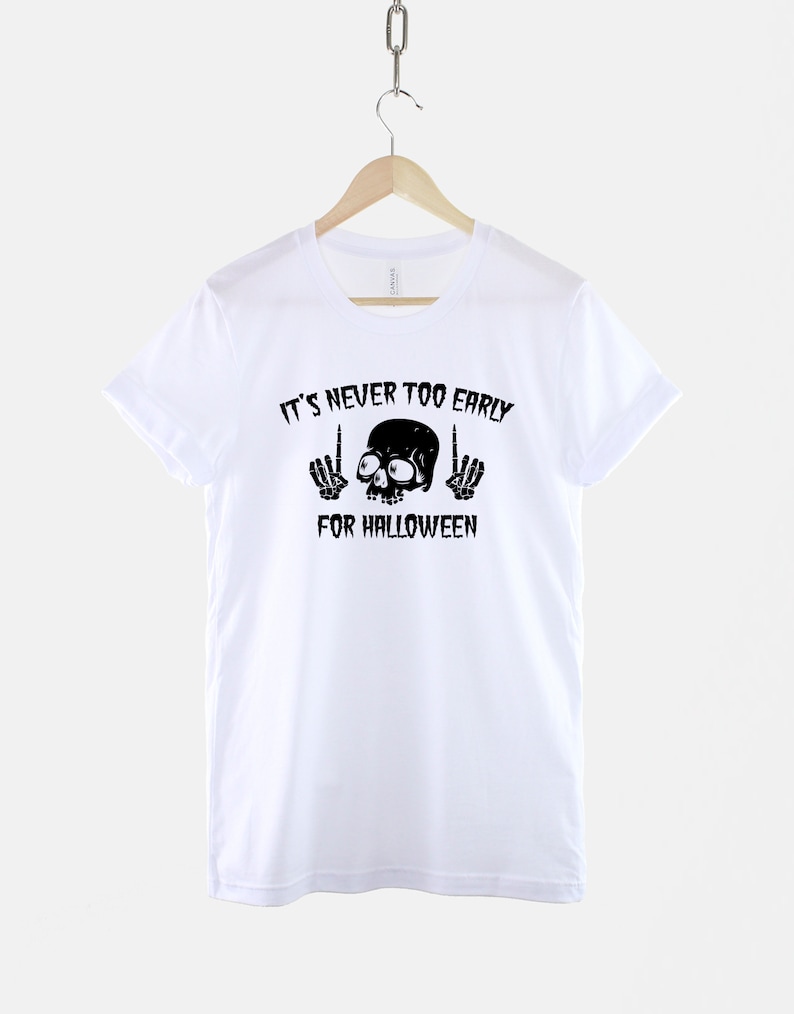 Peut inclure: T-shirt blanc avec un motif de cr&acirc;ne et d'os crois&eacute;s noirs et le texte "It's never too early for Halloween".