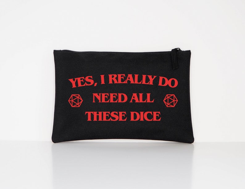 Puede incluir: Bolsa con cremallera de lona negra con texto rojo que dice "YES, I REALLY DO NEED ALL THESE DICE" y un gr&aacute;fico de dados poli&eacute;dricos rojos. La bolsa es rectangular y tiene una cremallera negra.