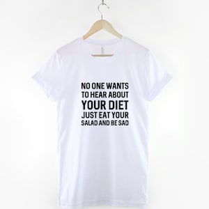 May include: White t-shirt with black text that reads "NO ONE WANTS TO HEAR ABOUT YOUR DIET JUST EAT YOUR SALAD AND BE SAD".