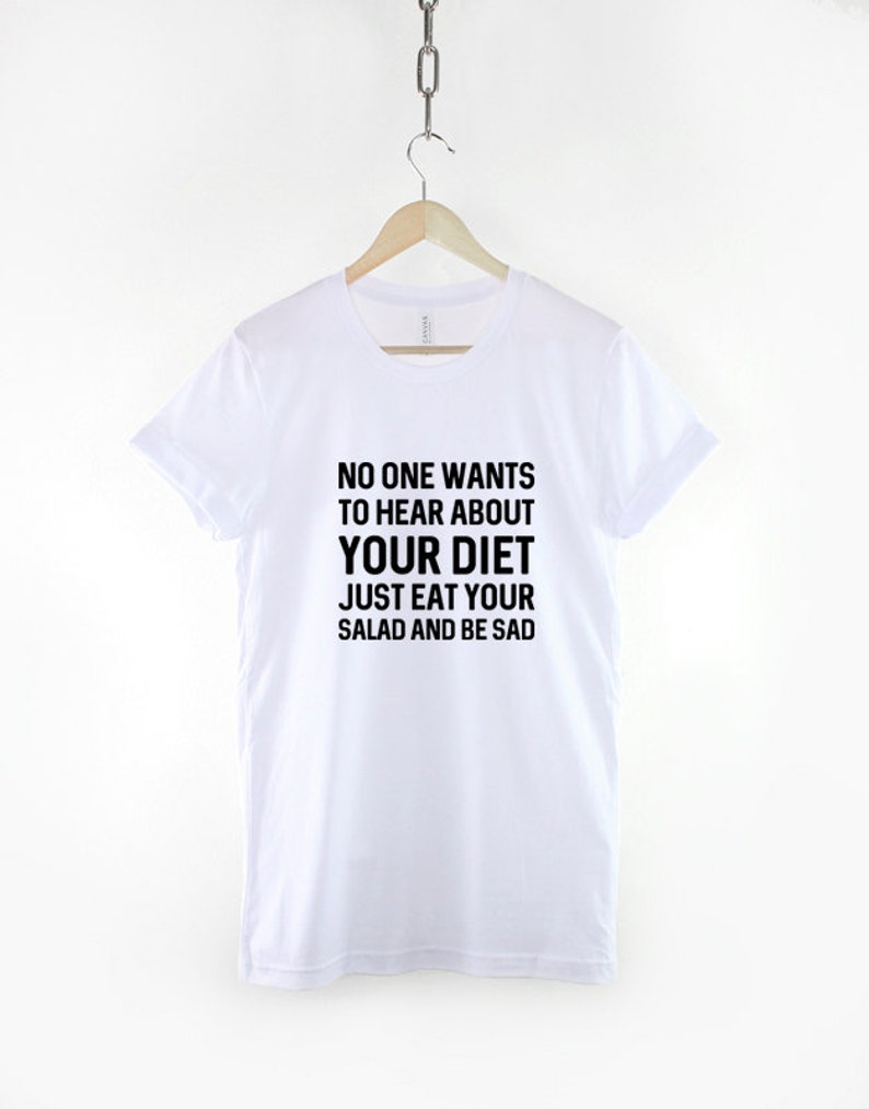 May include: White t-shirt with black text that reads "NO ONE WANTS TO HEAR ABOUT YOUR DIET JUST EAT YOUR SALAD AND BE SAD".