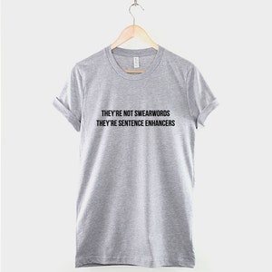 Puede incluir: Una camiseta gris jaspeada con el texto "They're not swearwords they're sentence enhancers" impreso en negro.