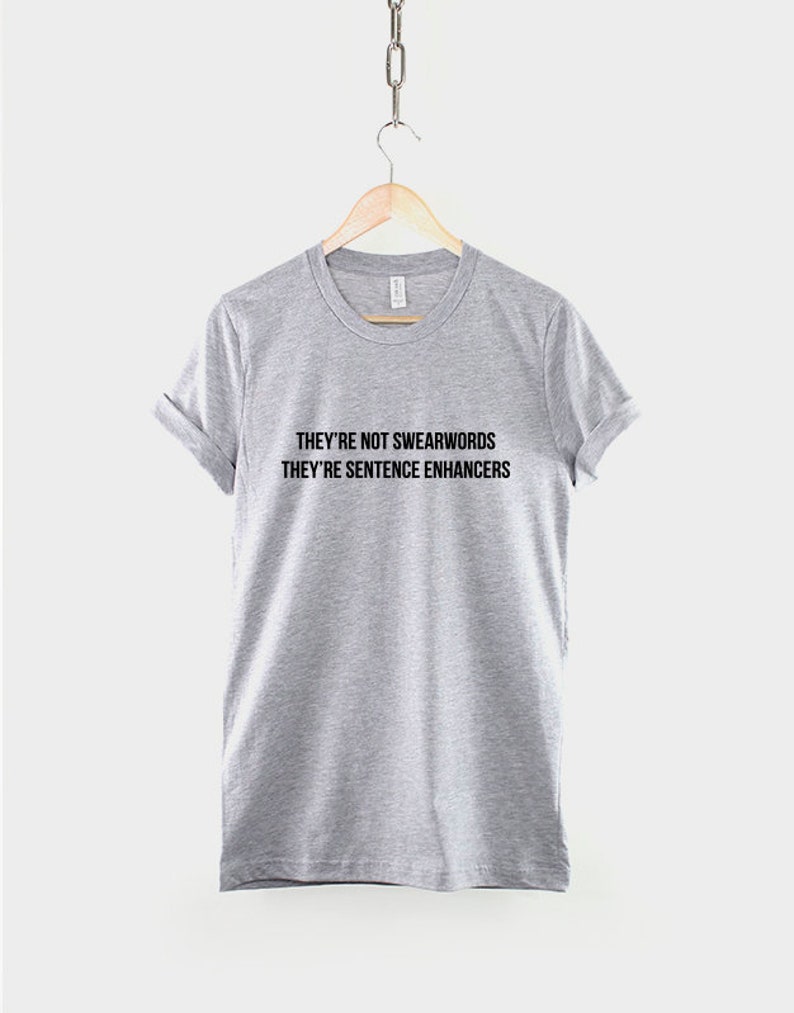 Puede incluir: Una camiseta gris jaspeada con el texto "They're not swearwords they're sentence enhancers" impreso en negro.