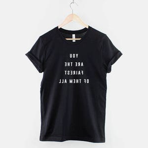 May include: Black t-shirt with white text that reads "Of the moment, Fair,  Are the, Uoy" printed backwards. The text is printed in a mirror effect.