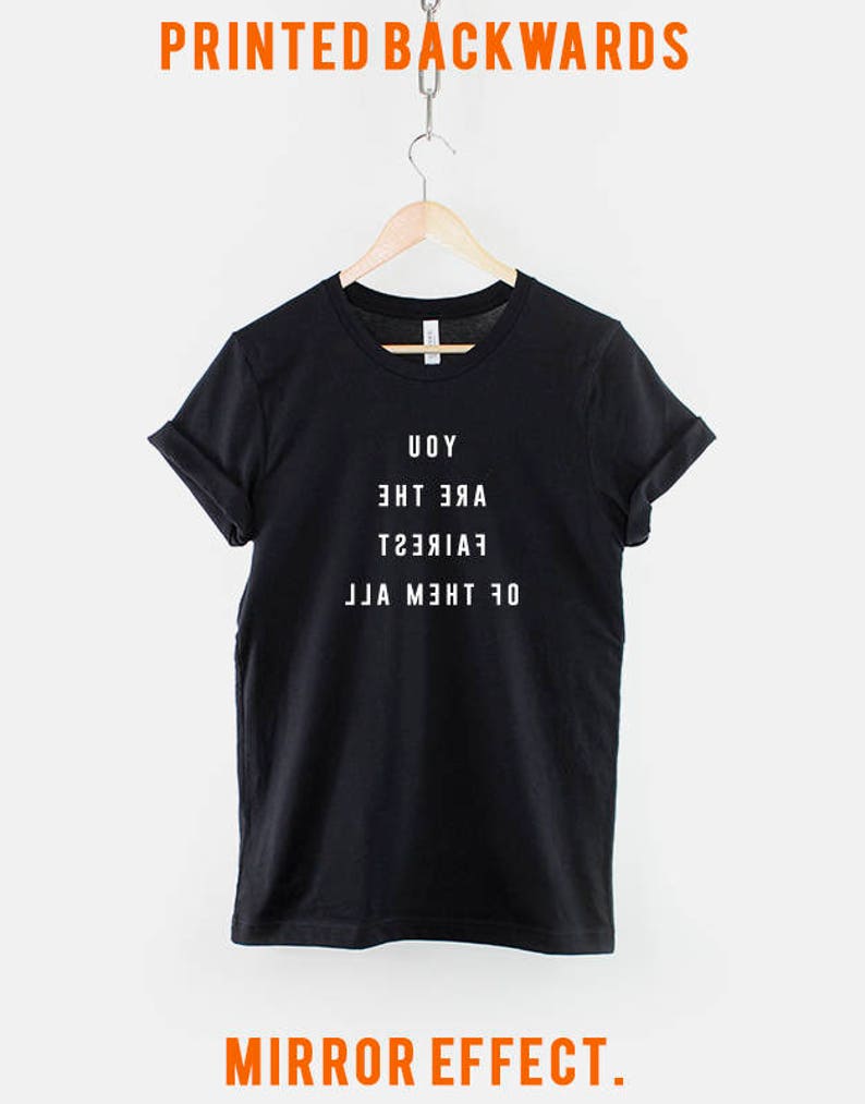 May include: Black t-shirt with white text that reads "Of the moment, Fair,  Are the, Uoy" printed backwards. The text is printed in a mirror effect.