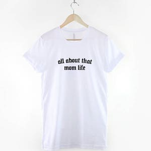 May include: White t-shirt with black text that reads "all about that mom life" in a gothic font.