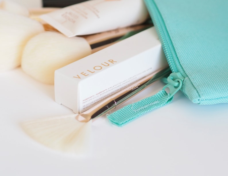 May include: A white makeup brush set with a turquoise zippered pouch. The brush set includes a large powder brush, a smaller brush, and a fan brush. The pouch has the word "VELOUR" printed on it.