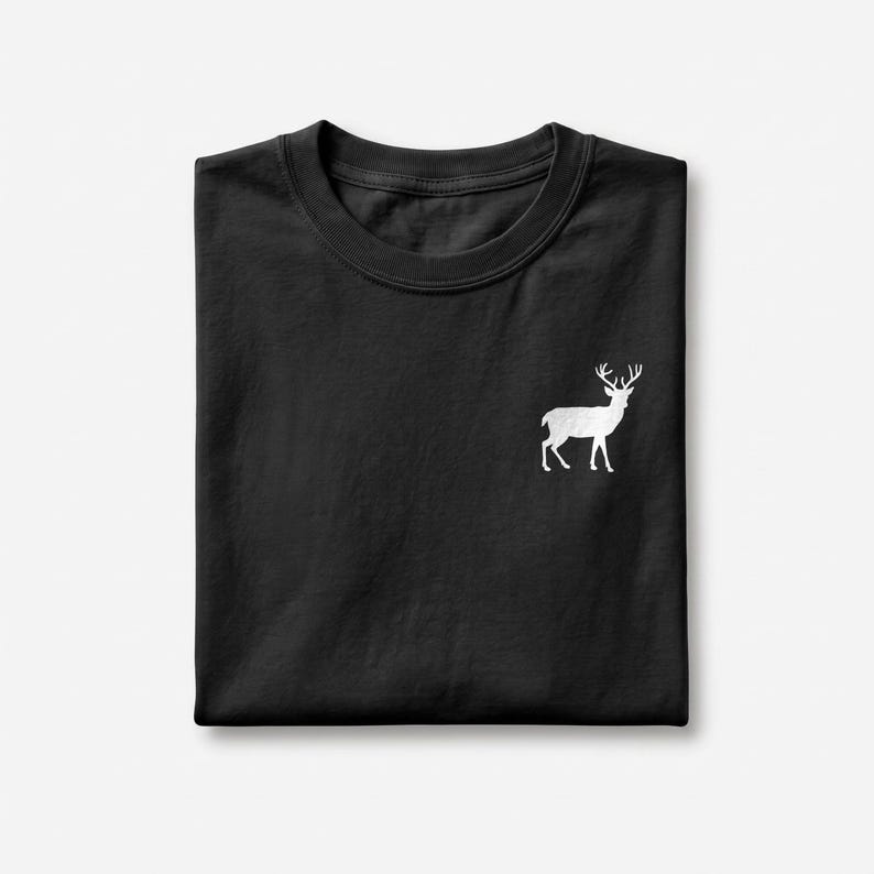 Puede incluir: Una camiseta negra de manga corta con un peque&ntilde;o gr&aacute;fico blanco de un ciervo de pie con astas, situado en la parte superior derecha del pecho. La prenda est&aacute; doblada cuidadosamente, mostrando un cuello redondo y un tejido negro liso.