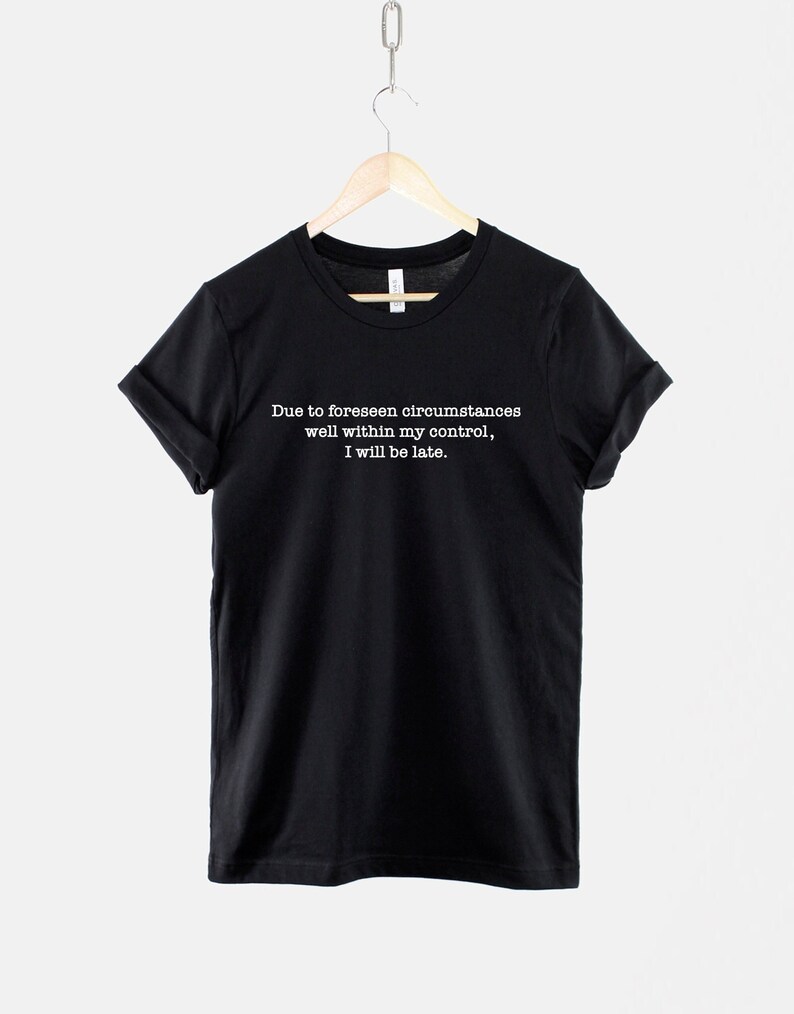 Op de afbeelding: Zwart T-shirt met witte tekst die luidt: "Due to foreseen circumstances well within my control, I will be late."
