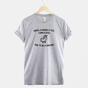 May include: Gray t-shirt with a black and white illustration of a unicorn and the text "Being a human is too complicated. Time to be a unicorn."