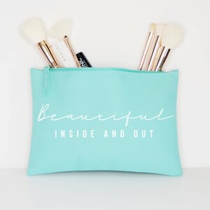 May include: A light blue zippered makeup bag with the text "Beautiful Inside and Out" in white. The bag is filled with makeup brushes.