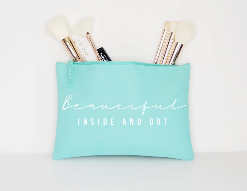 May include: A light blue zippered makeup bag with the text "Beautiful Inside and Out" in white. The bag is filled with makeup brushes.