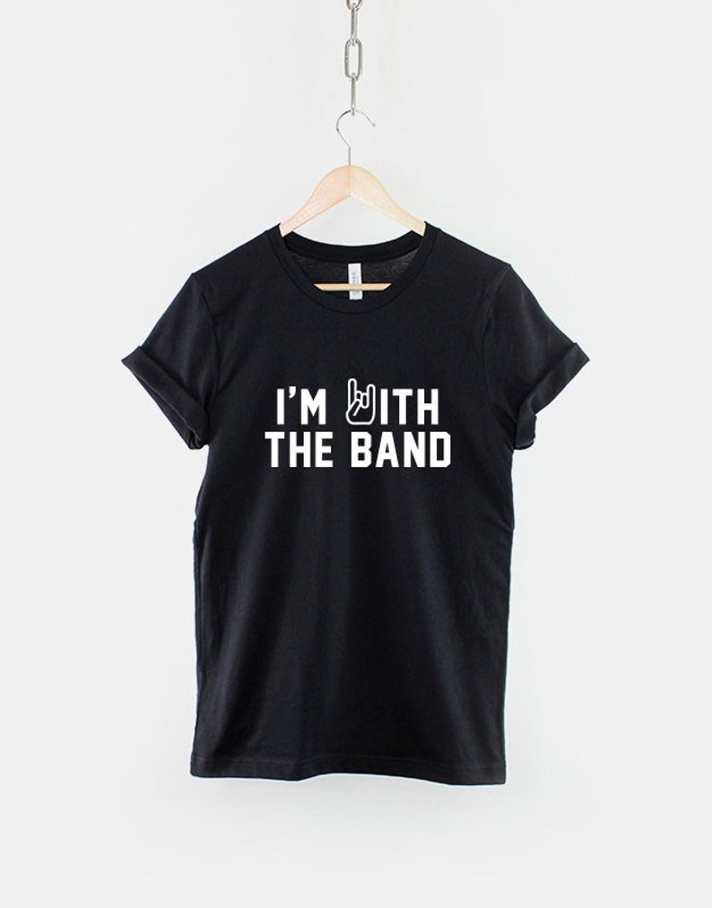 Puede incluir: Camiseta negra con texto blanco que dice "I'm with the band" y un gesto de mano de rock and roll.