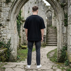 May include: A plain black short-sleeved t-shirt with a crew neckline paired with dark gray denim jeans and white sneakers. The outfit is shown from the back, featuring a relaxed fit for the shirt and a straight-leg cut for the denim trousers.
