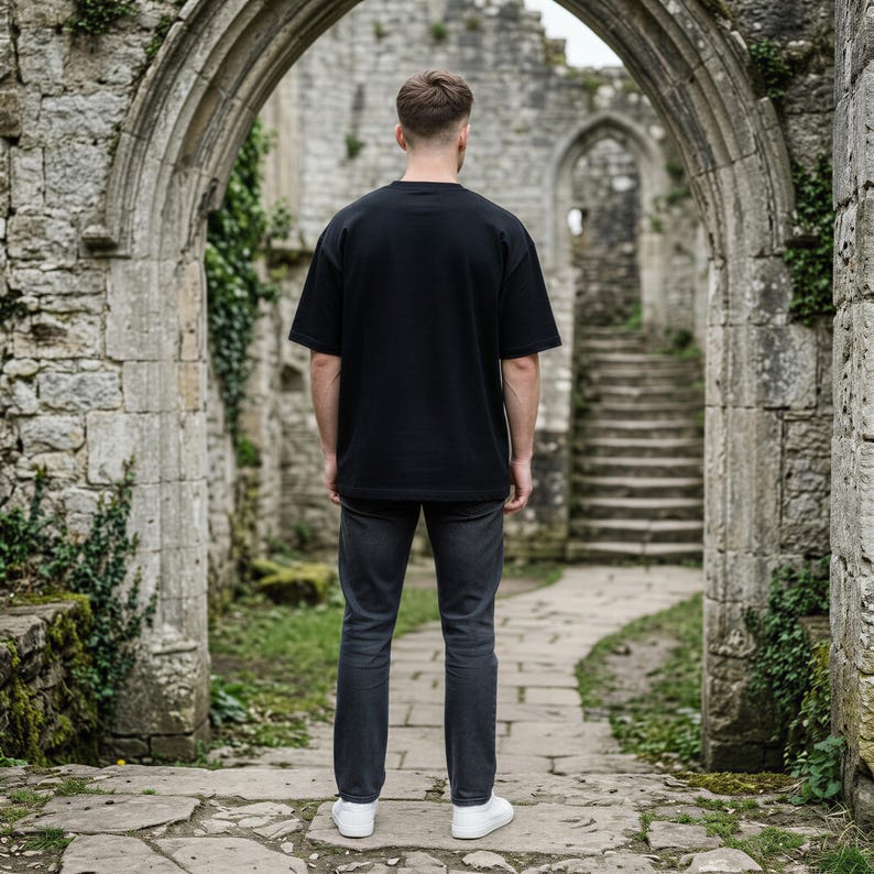 May include: A plain black short-sleeved t-shirt with a crew neckline paired with dark gray denim jeans and white sneakers. The outfit is shown from the back, featuring a relaxed fit for the shirt and a straight-leg cut for the denim trousers.