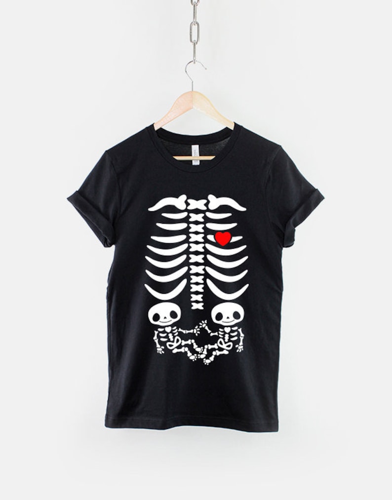 May include: Black t-shirt with a white skeleton graphic. The skeleton has a red heart in the chest area and two smaller skeletons in the stomach area.