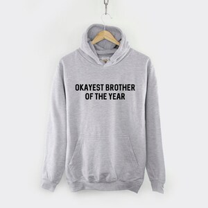 May include: A gray hooded sweatshirt with the text "Okayest Brother of the Year" printed in black.