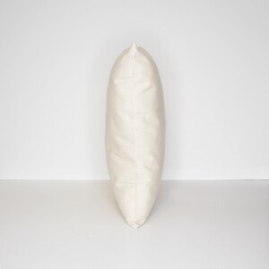 May include: A plain white pillow with a smooth, even surface. The pillow is standing upright on a white background.
