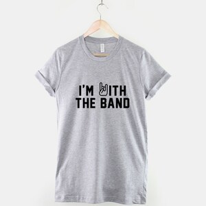 Puede incluir: Una camiseta gris con el texto "I'M WITH THE BAND" en letras negras y un s&iacute;mbolo de gesto de mano de rock and roll.