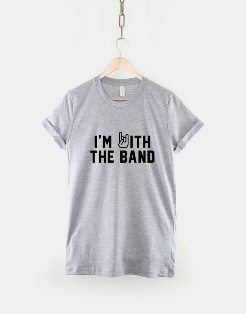 Puede incluir: Una camiseta gris con el texto "I'M WITH THE BAND" en letras negras y un s&iacute;mbolo de gesto de mano de rock and roll.