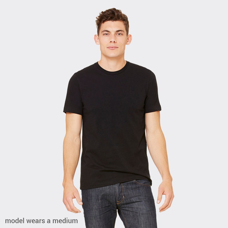 Puede incluir: Una camiseta negra de manga corta en un maniqu&iacute;. El maniqu&iacute; lleva pantalones vaqueros azules. "model wears a medium" est&aacute; escrito en la parte inferior de la imagen.