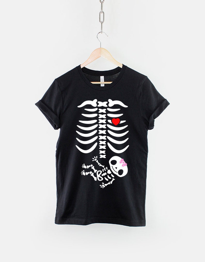 May include: Black t-shirt with a white skeleton graphic. The skeleton has a red heart in its chest and a small white skeleton baby in its belly with a pink bow.