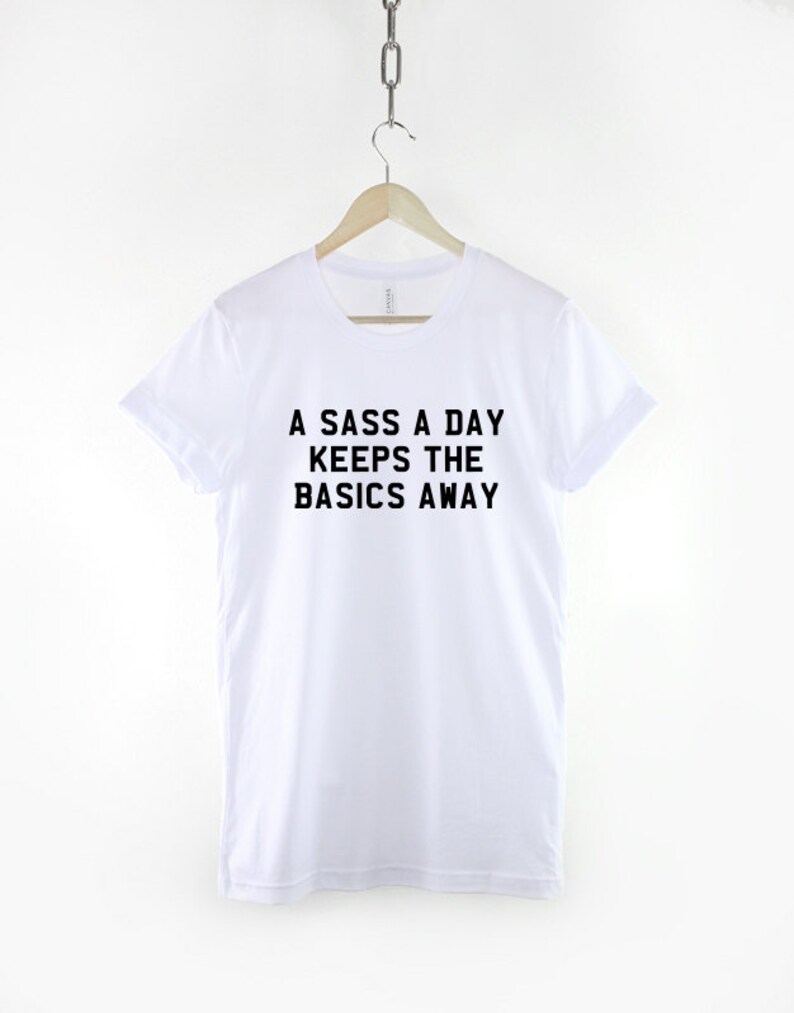 May include: White t-shirt with black text that reads "A sass a day keeps the basics away."