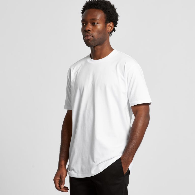 A man wearing a white t-shirt stands against a plain background.