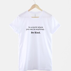 May include: White t-shirt with the text "In a world where you can be anything... Be Kind."