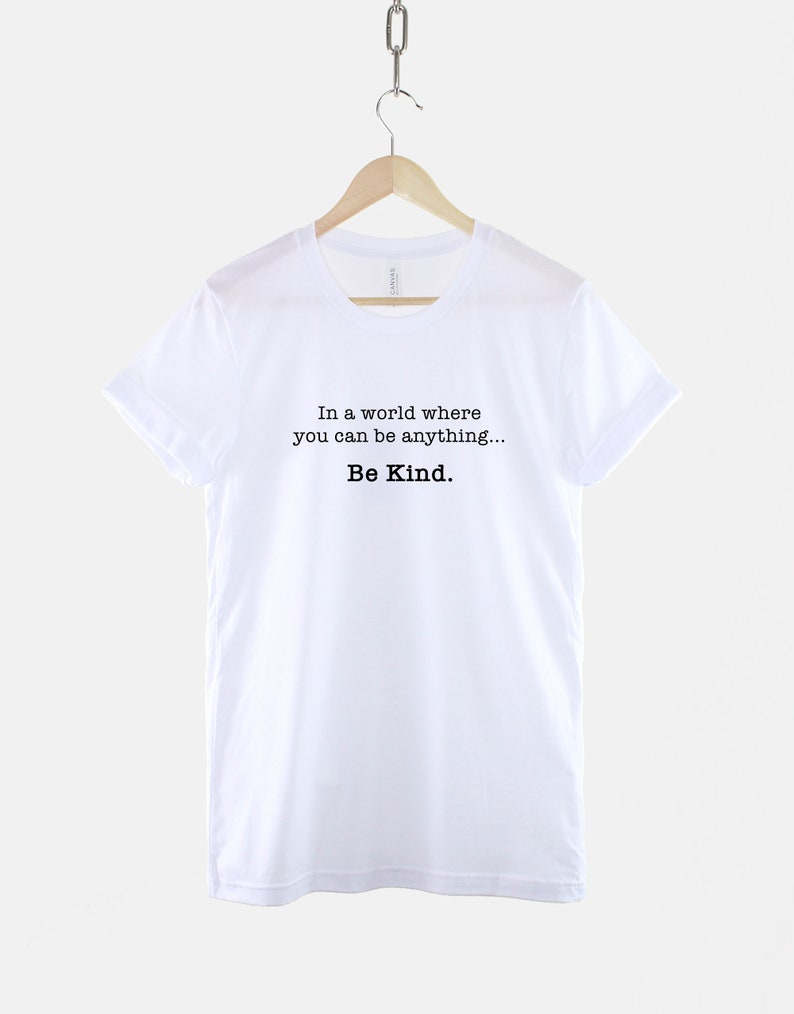 May include: White t-shirt with the text "In a world where you can be anything... Be Kind."