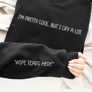 May include: Black sweatshirt with the text "I'M PRETTY COOL BUT I CRY A LOT." and "WIPE TEARS HERE" on the sleeve.