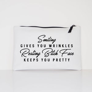 May include: White canvas zippered pouch with black text that reads "Smiling gives you wrinkles, Resting Bitch Face keeps you pretty." The pouch has a black zipper and pull tab.